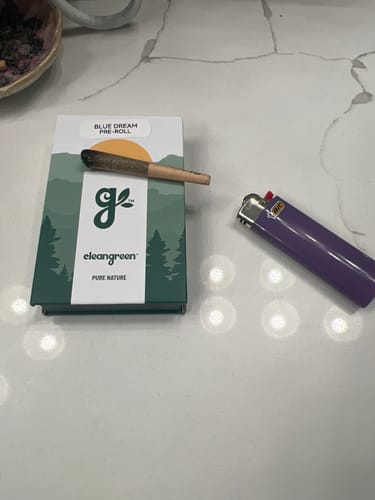 Reviewer's Grapes N’ Cream Pre-Roll on a product box next to a purple lighter on a white countertop.