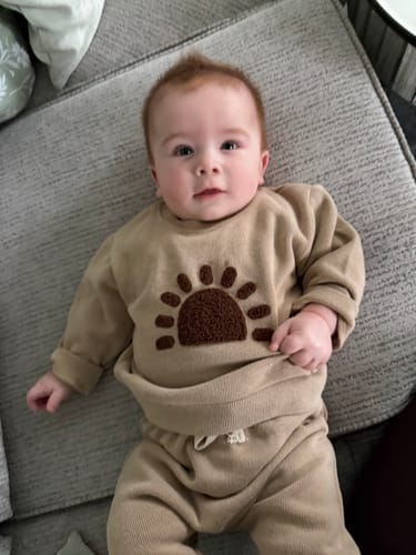 Customer's baby lying down, wearing the beige Sunshine Set with its embroidered sun.