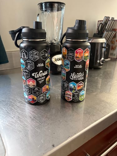 Customer's black '50 States Of The USA' water bottle next to their 'World Explorer' bottle on a counter.