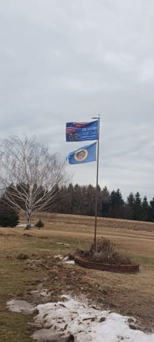 Customer's old style State of Minnesota flag flying outdoors on a flagpole in a windy field.