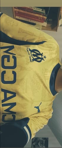 Gros plan du maillot 25/26 Marseille Fourth jaune porté par un client, montrant l'écusson.