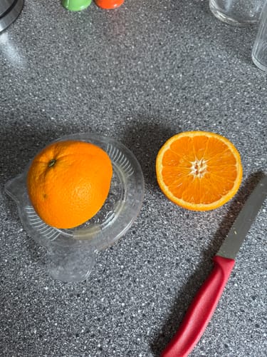 Ein Kunde zeigt eine aufgeschnittene, leuchtende Orange aus der Box auf einer Saftpresse.