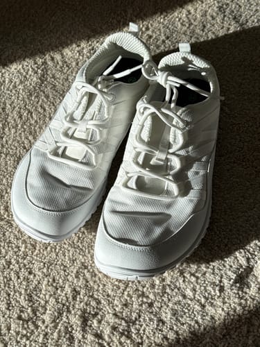 Rezensent zeigt seine weißen Forestep Ⅰ Barfußschuhe auf einem Teppich.