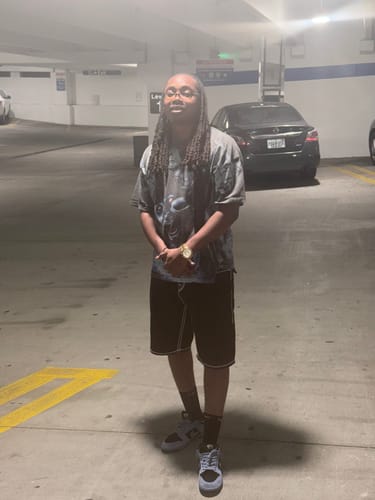 Reviewer in a parking garage, wearing a grey graphic tee, dark shorts, and sneakers.