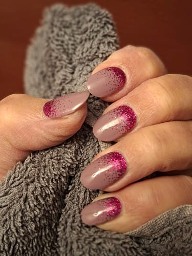 Kundin zeigt ihre Nägel mit dem 'Time To Party' UV-Gel-Design, das einen Ombré-Verlauf von Nude zu pinkem Glitzer zeigt.
