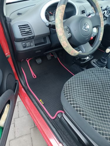 Opinia klienta przedstawiająca czarny dywanik samochodowy z różowym obszyciem, idealnie dopasowany do podłogi po stronie kierowcy.