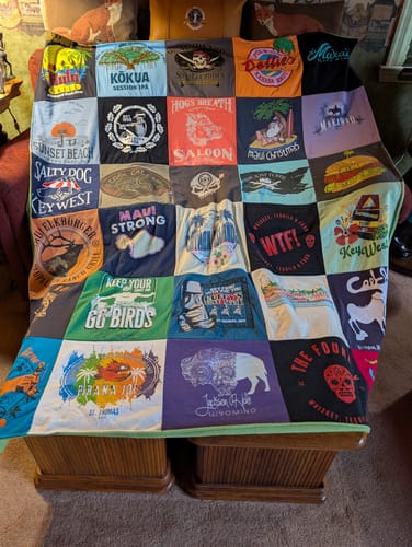 Customer's custom Project Repat T-Shirt Quilt with many colorful shirt panels, shown draped over a bench.
