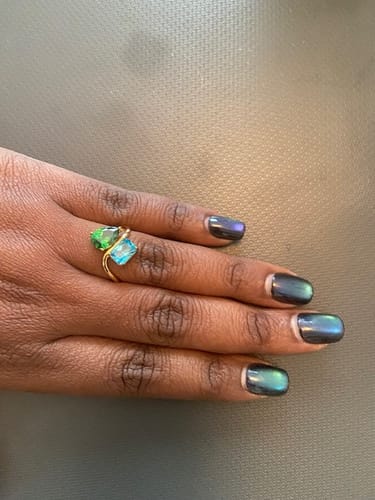 Reviewer's hand wearing the Navae Birthstone Ring, showing the curved gold band with a green and a light blue stone.