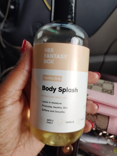 A reviewer's hand holding a clear bottle of the yellow Vanilla Drip Body Splash hydrating oil.