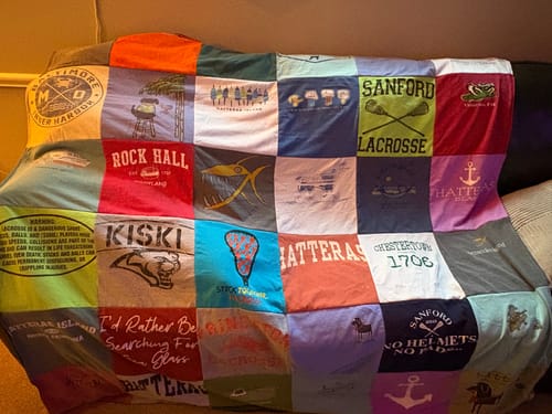 Customer's colorful Project Repat T-Shirt Quilt, made from many t-shirts with unique logos, draped over a couch.