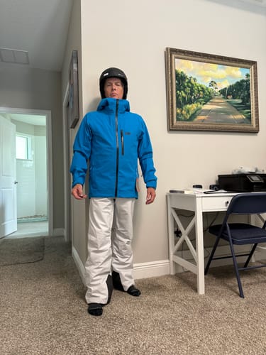 Reviewer wearing the blue Helly Hansen Swift 3L Shell Ski Jacket with the hood up over a helmet indoors.
