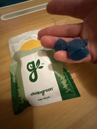 Reviewer's hand holding two blue Create Gummies over the product packaging on a wooden table.