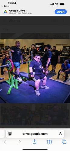 Reviewer wearing a black ratcheting belt and wristbands while sitting on a bench press at a competition.