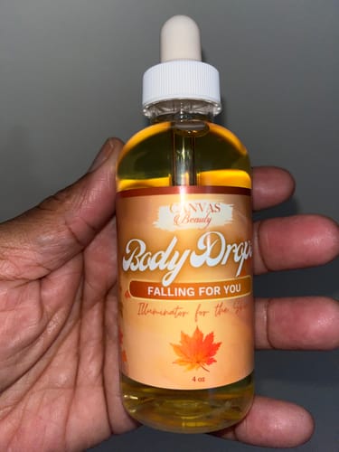 Customer's hand holding a clear dropper bottle of golden Body Drops: Falling For You oil.