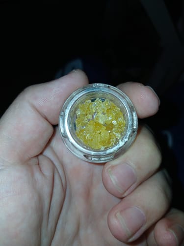 Customer holding a small open jar of golden, crystalline Live Resin THCa Diamonds in their palm.