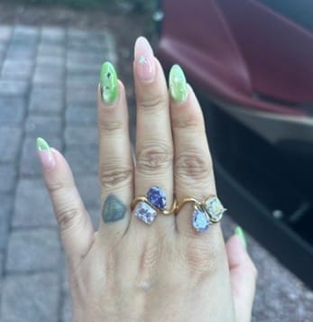 Customer's hand wearing two gold Navae Birthstone Rings with colorful purple and blue stones.
