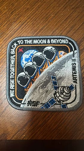 Customer's Artemis II Collectors Patch on a wooden surface, showing the detailed embroidered design of astronauts and a spacecraft.
