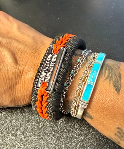Reviewer wearing the black and orange Hard Days Paracord Bracelet, stacked with other jewelry on their wrist.