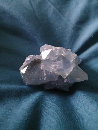 La géode de Célestine d'un acheteur, un amas de cristaux bleu clair reposant sur un tissu bleu.