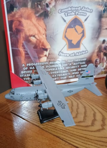 Customer's Postage Stamp C-130 model airplane displayed on its stand on a wooden shelf.