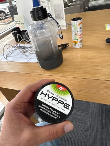 Customer holding a black can of HYPPE Chewy Watermelon moist nicotine pouches over a wooden desk.