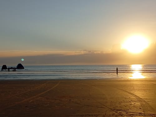 Foto da avaliação do cliente para a Camisola Flor Rosa, mostrando uma praia ao pôr do sol.