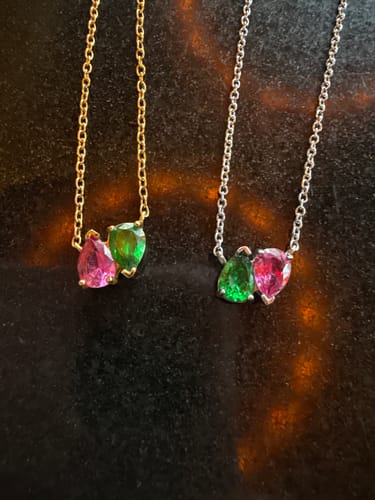 Customer's two Elara Birthstone Necklaces, one with a gold chain and one with a silver chain, on a dark surface.