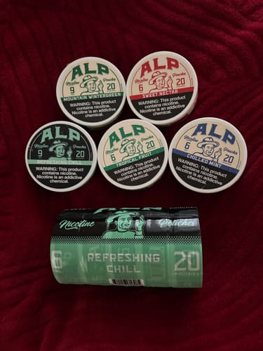 Reviewer's collection of ALP nicotine pouches, showing a roll of Refreshing Chill and tins of other flavors.