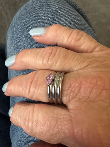Reviewer wearing the Cassie Birthstone Ring with a pink stone on their middle finger against a denim background.