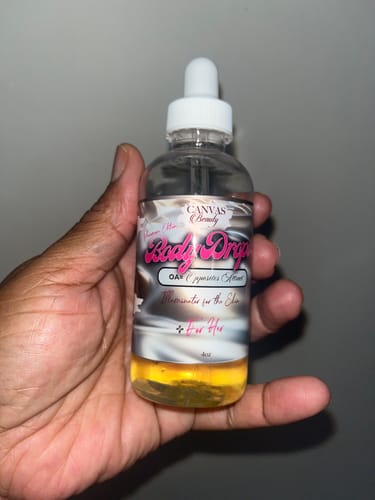 Customer holds a clear 4oz bottle of the golden Body Drops: Pheromone Female oil.