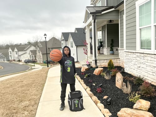 Customer wearing the black custom basketball jersey with a matching backpack outdoors, holding a basketball.