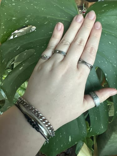 Customer's hand wearing several silver-colored rings and bracelets from the jewelry bundle against a large leaf.