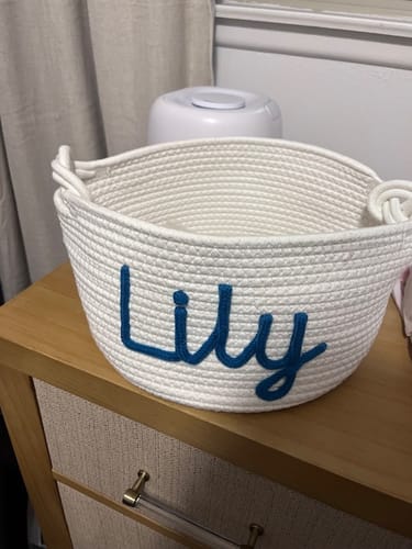 Customer's white personalized knitted basket sitting on a wooden surface, with the name 'Lily' in blue script.