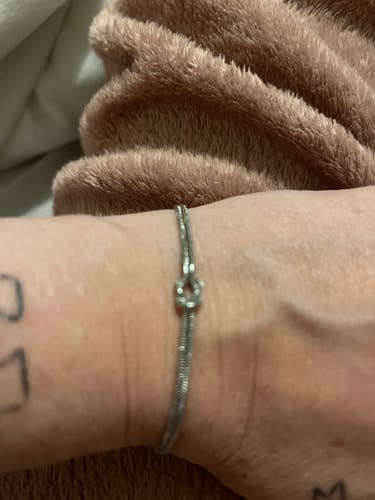 Close-up of a customer wearing a thin, silver-colored bracelet with a knot design on their wrist.