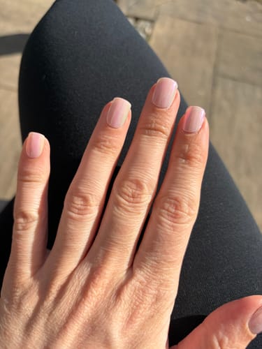 Hand einer Kundin mit einer gepflegten, hellrosa Maniküre durch die UV-Gel-Nagelfolien 'Pink Champagne'.