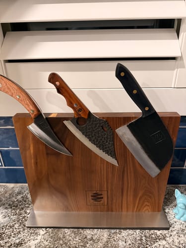 Reviewer's walnut magnetic knives holder on a counter, holding three cleaver-style knives at an angle.