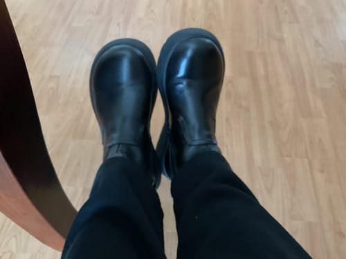A reviewer's point-of-view showing their black platform boots worn with black pants indoors.