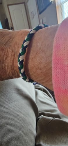 Close-up of a customer wearing their woven DAVID Bracelet with blue, green, and white strands on their wrist.