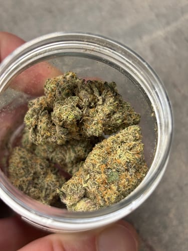 Reviewer's close-up of several green Happy Weedz THCA Flower buds in an open glass jar.
