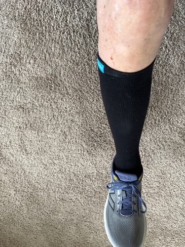 A reviewer's leg shown from above wearing a black Performance Eucalyptus Compression Sock with a gray sneaker.