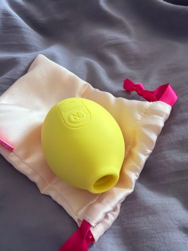 Customer's yellow Lem Clitoral Massager resting on its light pink satin storage bag.