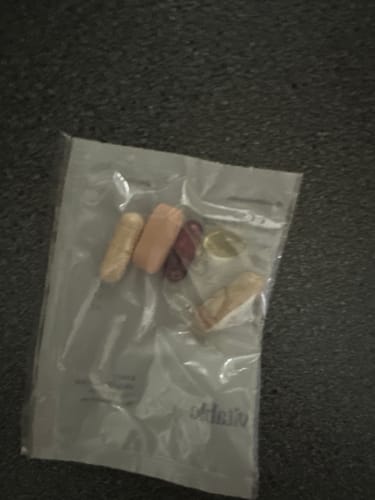 Reviewer showing a clear daily-dose packet containing an Astaxanthin capsule alongside other supplements.
