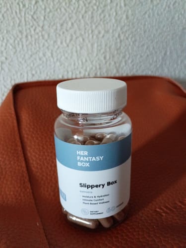 Customer's clear bottle of Slippery Box capsules with a white and blue label, sitting on a brown surface.