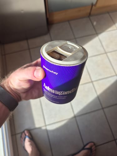 Un client tient dans sa main le pot violet d'Ashwagandha ouvert, révélant les gélules à l'intérieur.