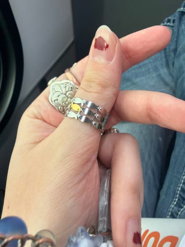 Customer's hand wearing the Swim Against The Current Ring on their thumb. The silver band has one unique gold fish.