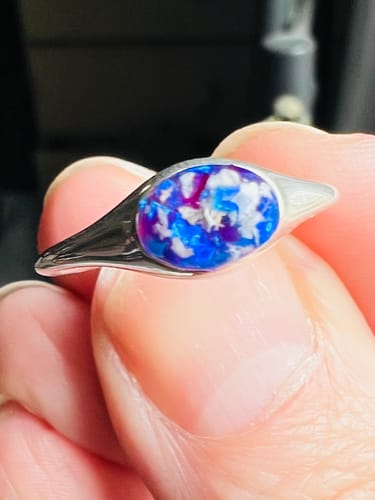 A reviewer holding their Silver Oval Ring, showing the blue and purple opal mixed with ashes.