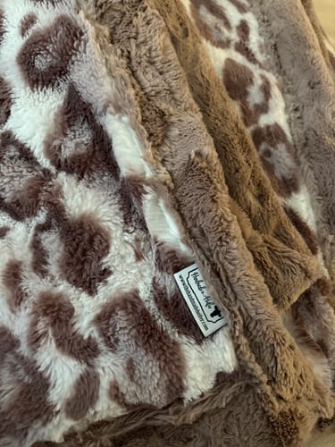 Reviewer's close-up of The Jungle Fig Blanket, showing the mauvy leopard print and solid textured sides with the brand tag visible.