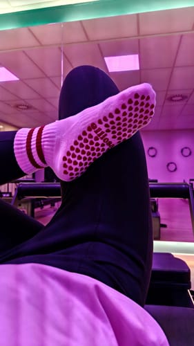 Reviewer in a studio shows the red grips on the sole of their white Dual-Direction Grip Stripes socks.