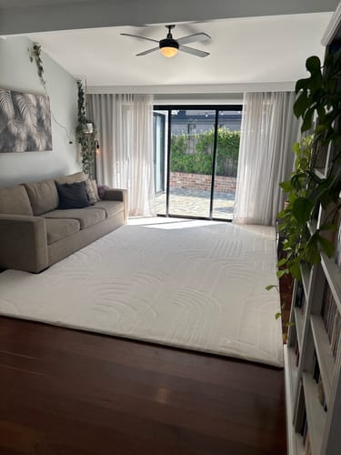 Customer's large white Mellow Mat on a dark wood floor in a living room.