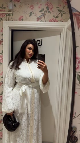 Reviewer takes a mirror selfie wearing the long, white lace Lunaria dress with matching belt.